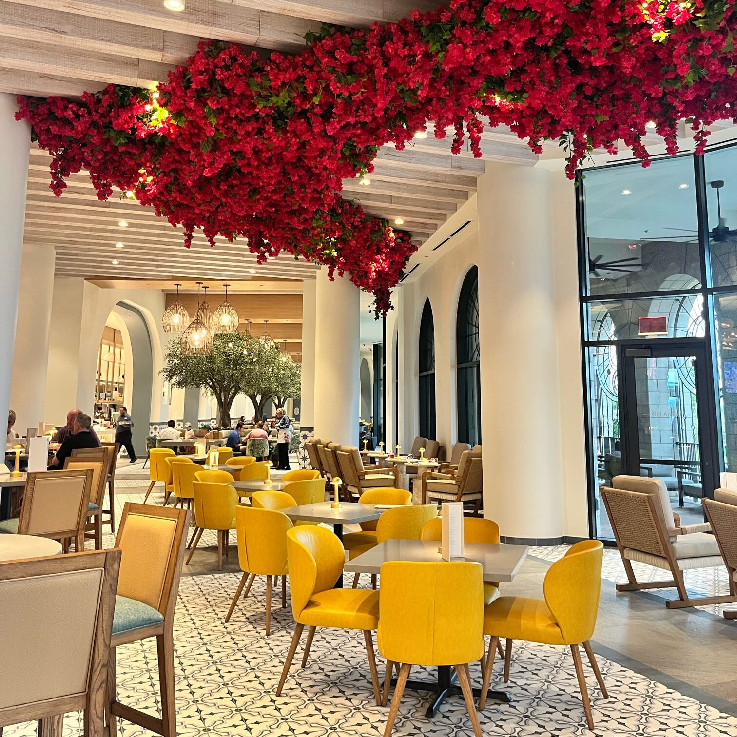 A modern dining area featuring yellow chairs and tables, with decorative red flowers hanging from the ceiling and a warm atmosphere.