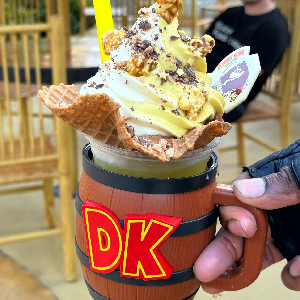 A dessert featuring soft-serve ice cream topped with popcorn and chocolate, served in a unique barrel-shaped cup labeled 'DK'.